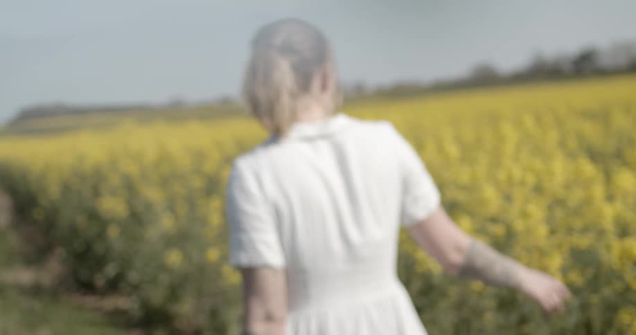 The woman walks along a field of yellow flowers