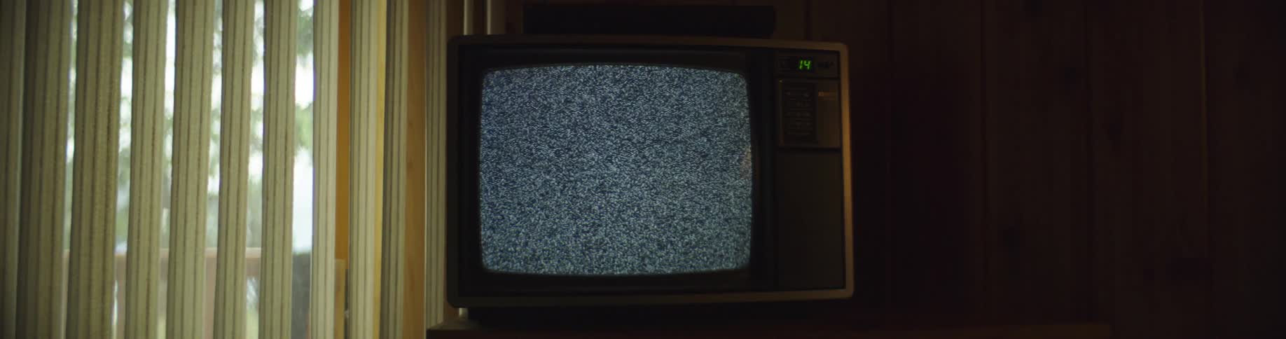 A person walks over to a television playing static and shuts it off