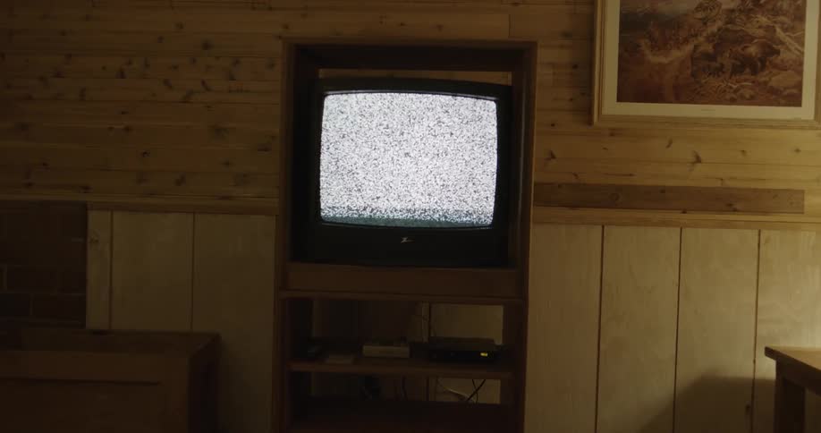 An old television displaying static in a living room with retro furniture and technology
