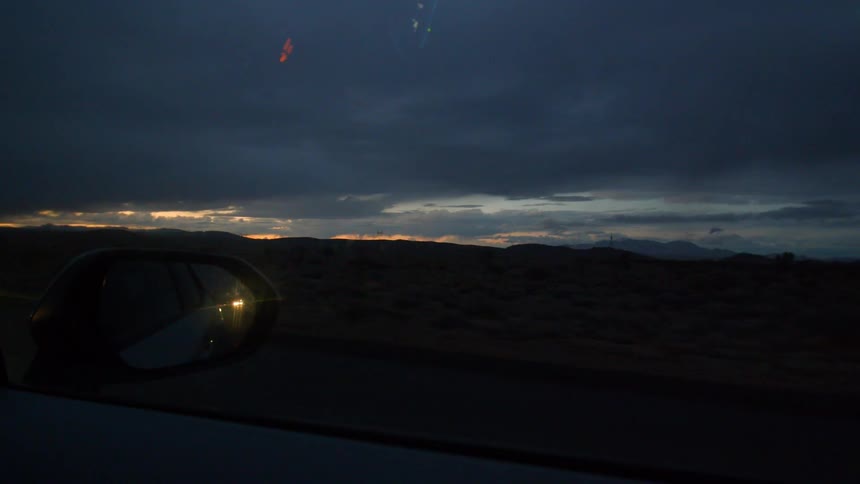 A car drives through a desert at dusk