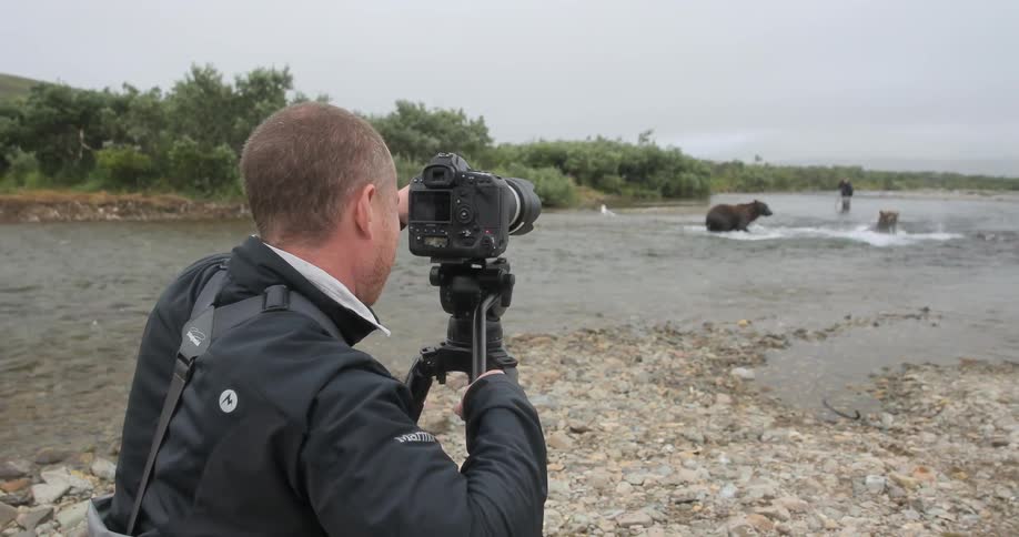 A man photographs bears splashing in a river in the wilderness