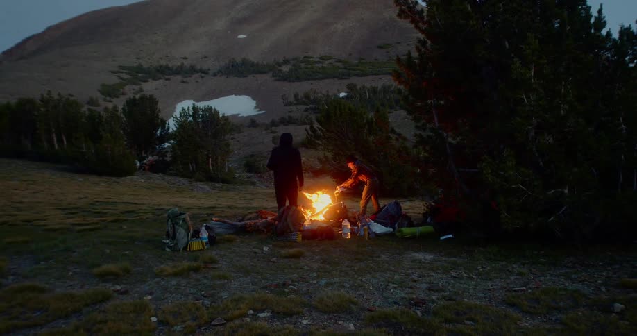 Two men build a campfire near the base of a hill