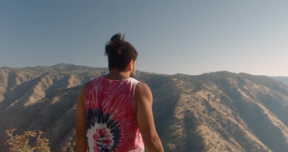 A man walking near a cliff with hills in the foreground