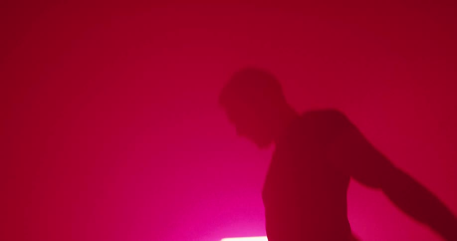 A man rapidly doing squats in a room dimly lit by a reddish light