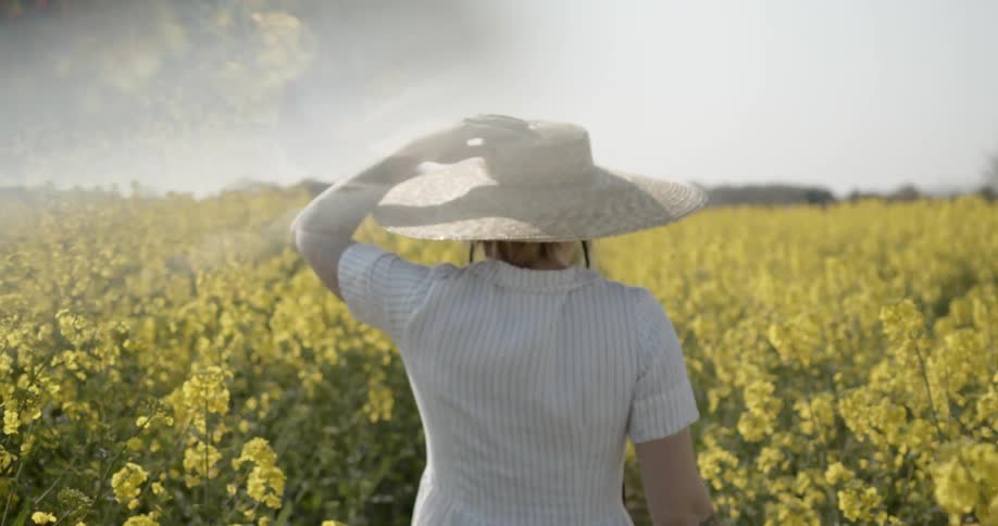 A woman with a hat walking through a field of flowers