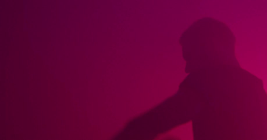 A silhouetted man lifts a kettlebell in a dark room with red lights