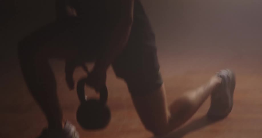 A white man does deep knee bends with a kettle ball