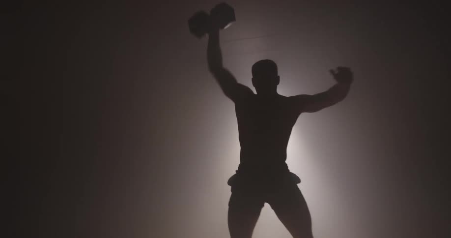 A man in a gymnasium lifting a dumbbell over his head