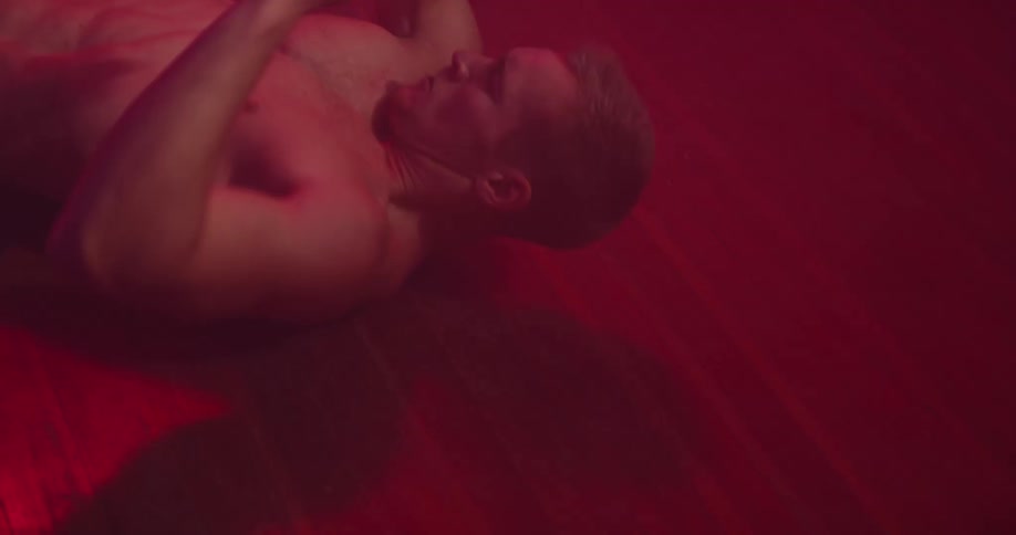 A man doing exercising with a barbell in a room illuminated by a dim red light
