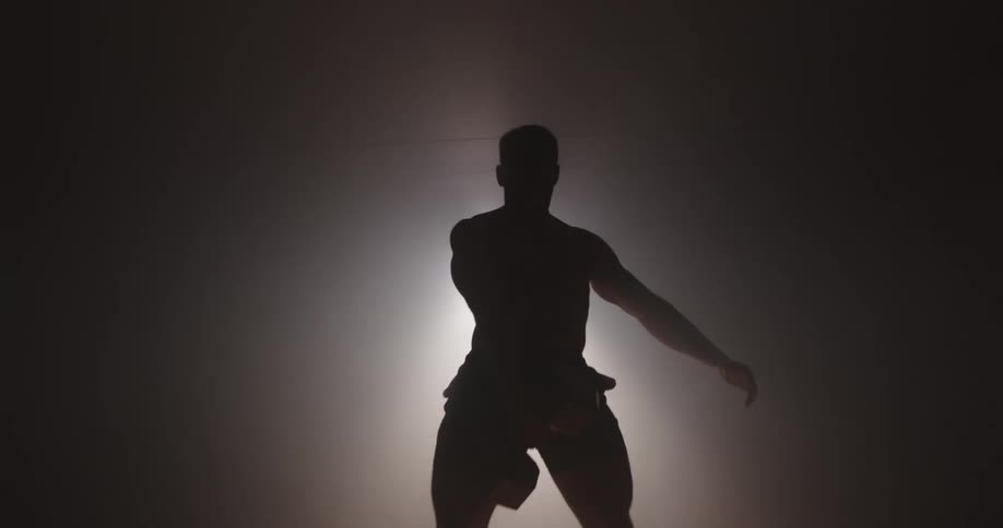 A silhouetted man exercises with a dumbbell in a dark room