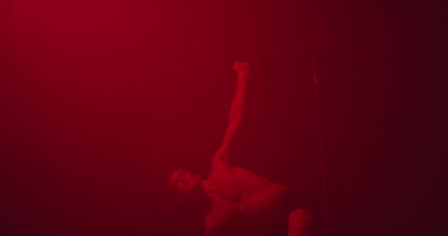 A man in a room with red light holding a dumbbell and standing up