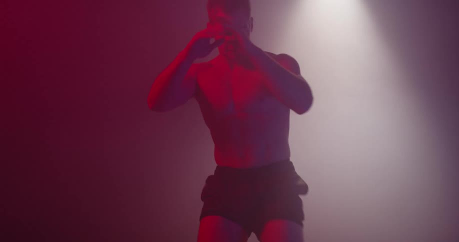 Man practices fighting moves under a spotlight in a foggy room