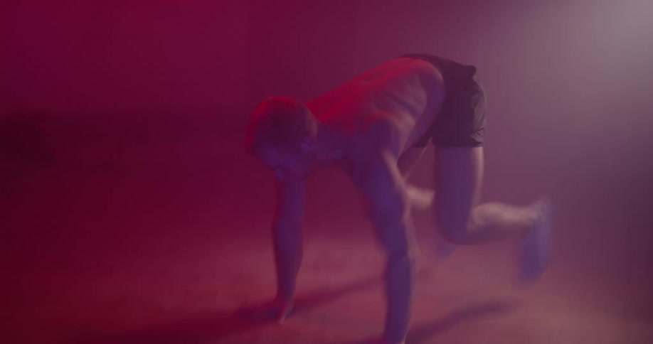 Shirtless man works out in a dimly lit room under a spotlight