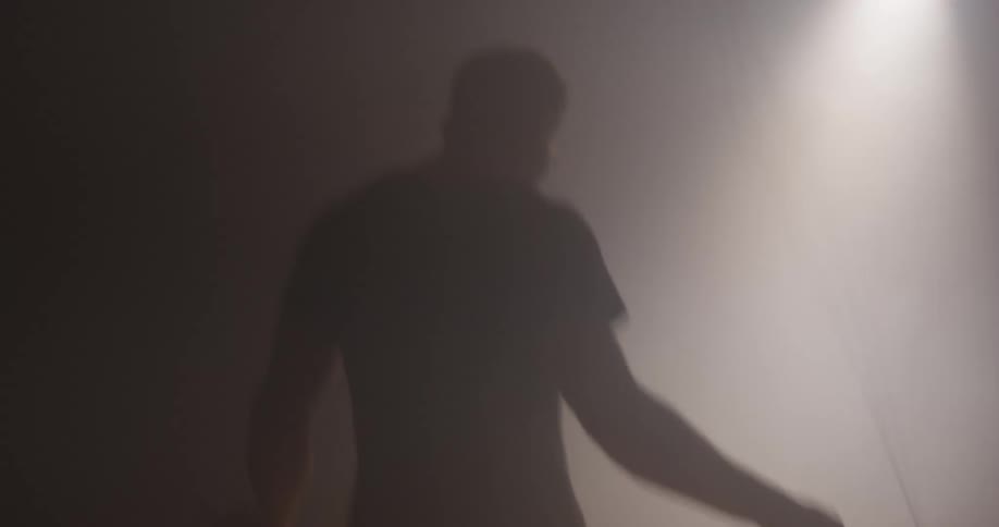 A man exercising with a jump rope in a dark room with a single distant light