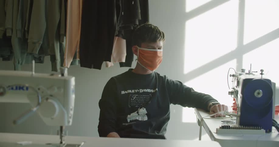 Man wearing orange face mask sits in front of sewing machine