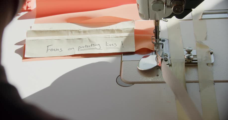 A man sews cloth masks using a pattern that has focus on saving lives written on it