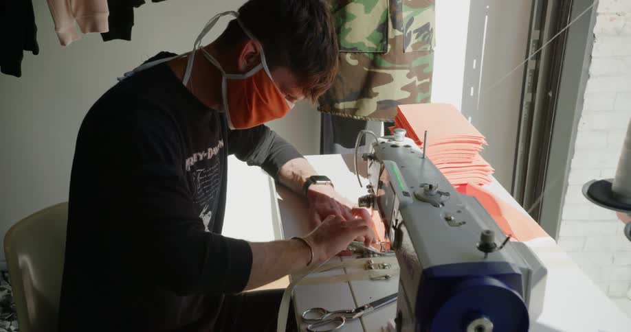 A teenage boy is sitting at a desk sewing masks