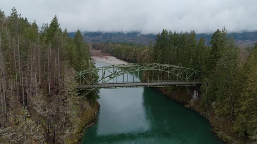 Two lane arch bridge spanning river through pine forest