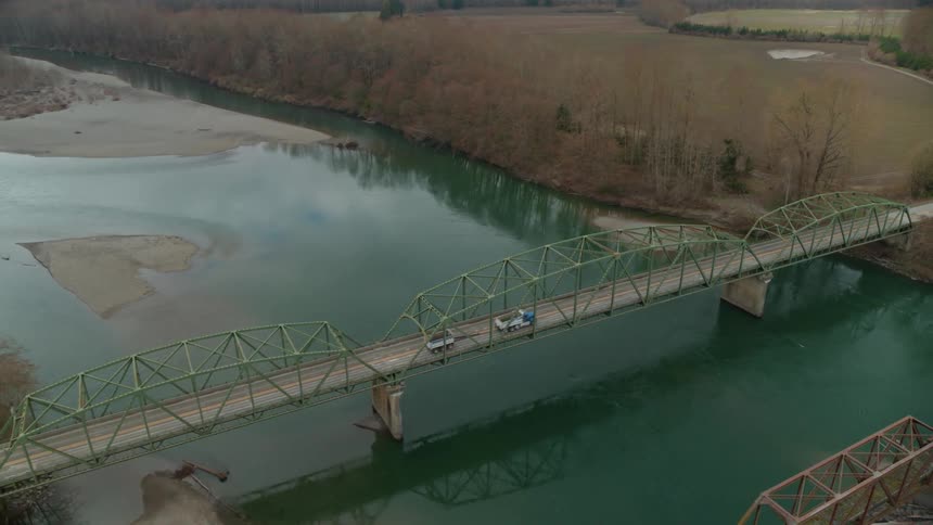 Cars travel across two lane rural bridge over river