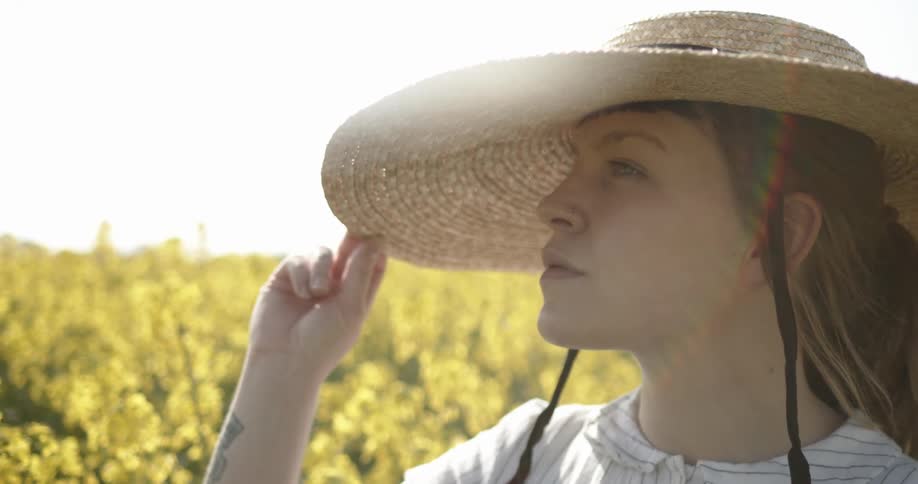 A woman stands in a field holding her sun hat