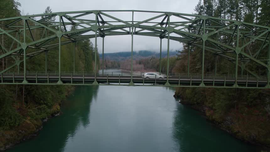 Cars cross bridge over river between forests as fog covers horizon