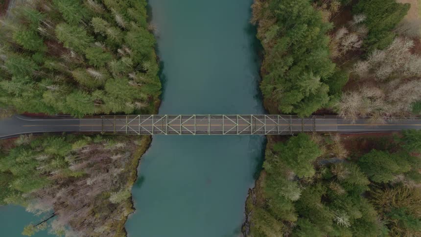 Birds eye view of two lane bridge spanning river in forest