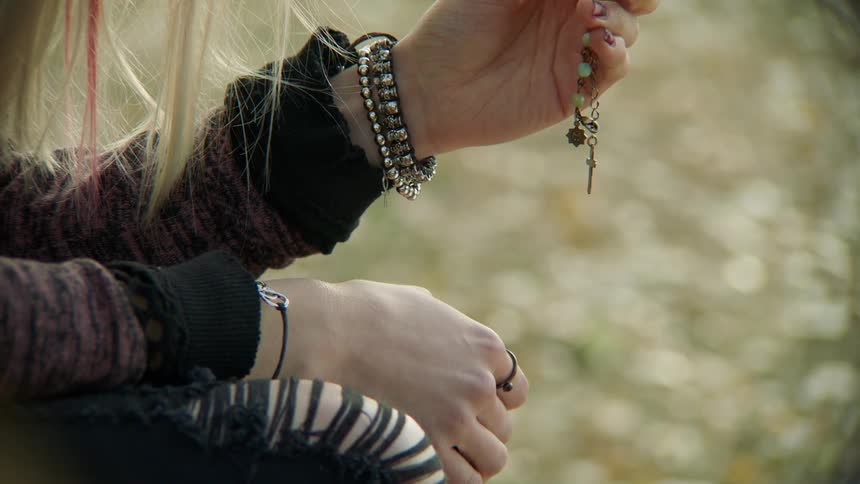 A white woman sits outdoors and fingers a rosary