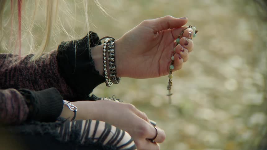 A teenager holds a cross on some beads and rubs it