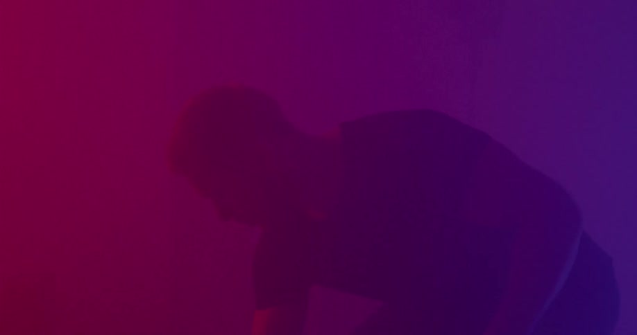 Man crouches down in pink and purple lighting