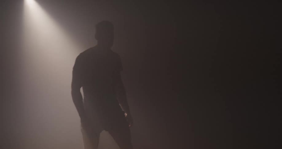 Silhouette of a man walking around a dimly lit foggy room