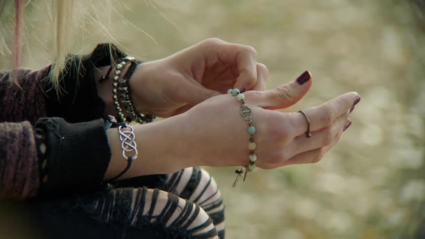 A white woman sits outdoors playing with a bead bracelet