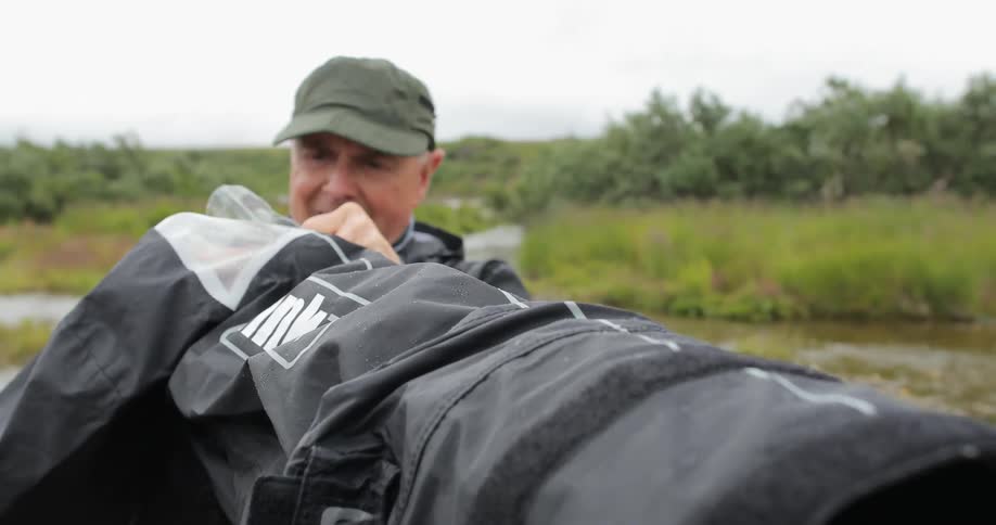 A man is unwrapping something by a stream on a rainy day