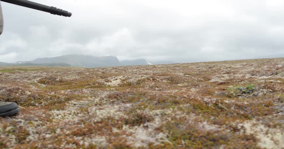 A man walks across a rocky area carrying a tripod