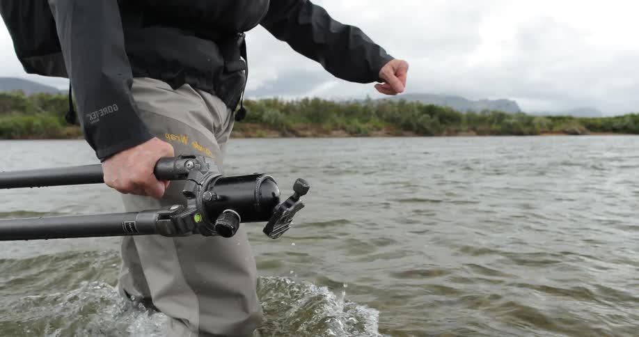 A photographer wades across a river with a tripod in hand