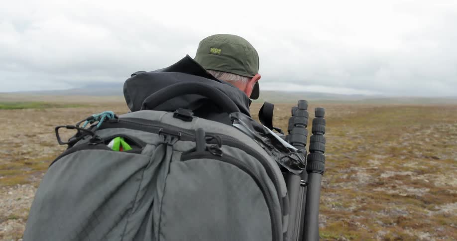 A man carrying gear on his back walks across field in the winter