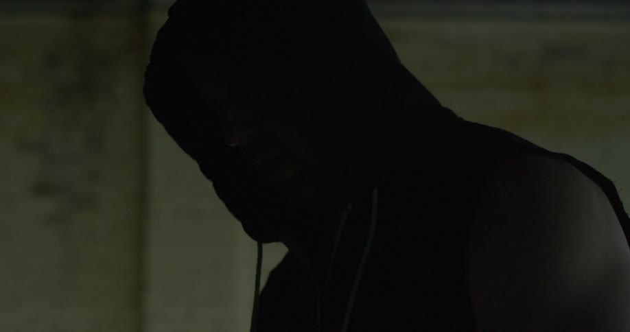 A man with a hood on his head standing in a dim room