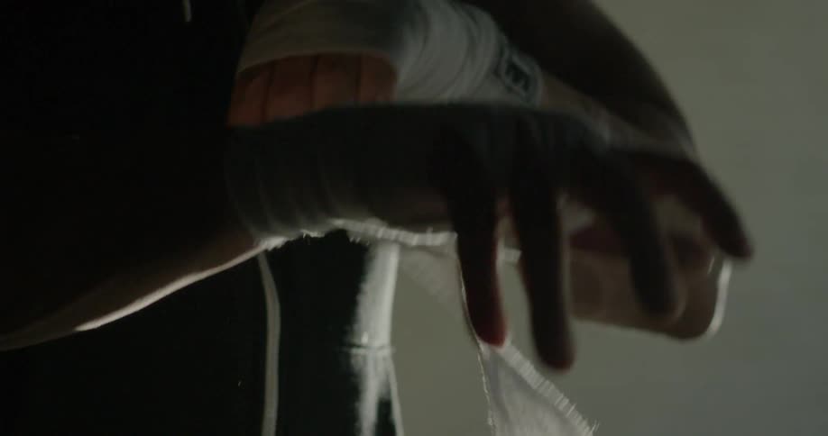 A man is wrapping his hands in a dark area