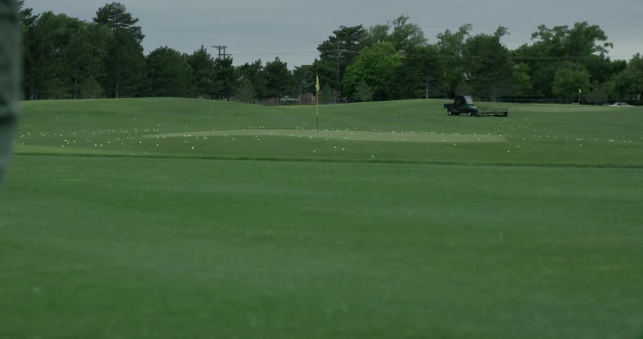 A golfer hits a ball on a golf course on an overcast day
