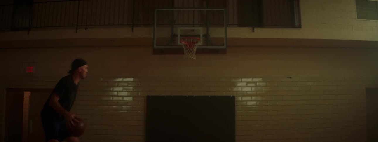 A white man dribbles a basketball and takes a shot in a gym