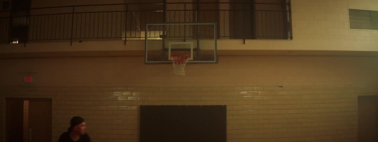 A man dribbles a basketball and shoots a hoop in a gym