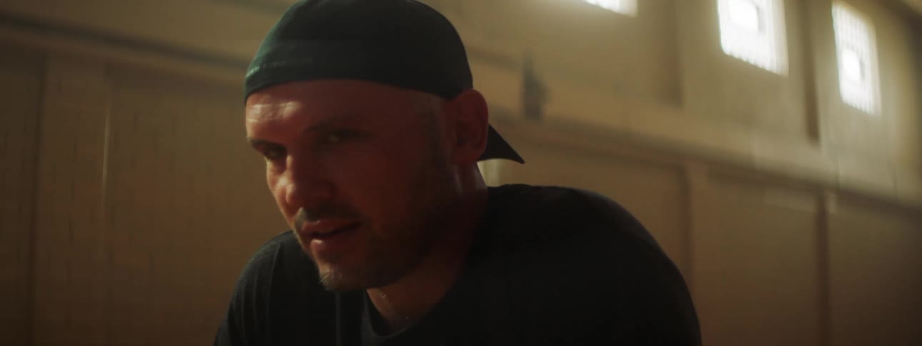 A man sitting indoors looking down before turning his head to smile into the camera