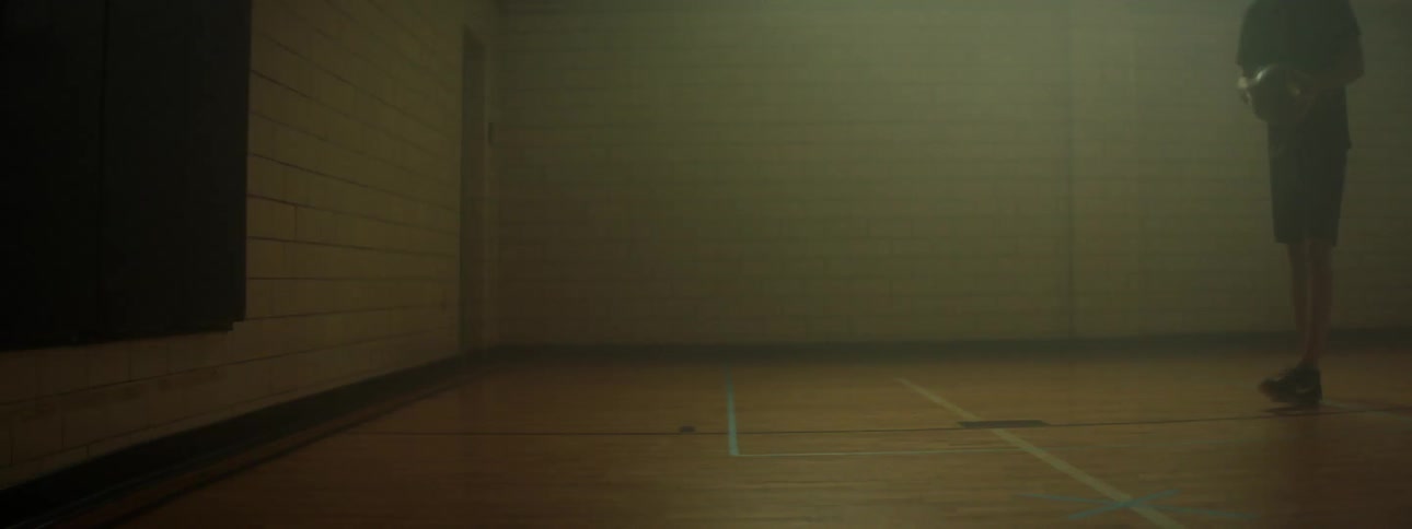 A man dribbling a basketball and preparing to make a shot in a small dimly lit gymnasium