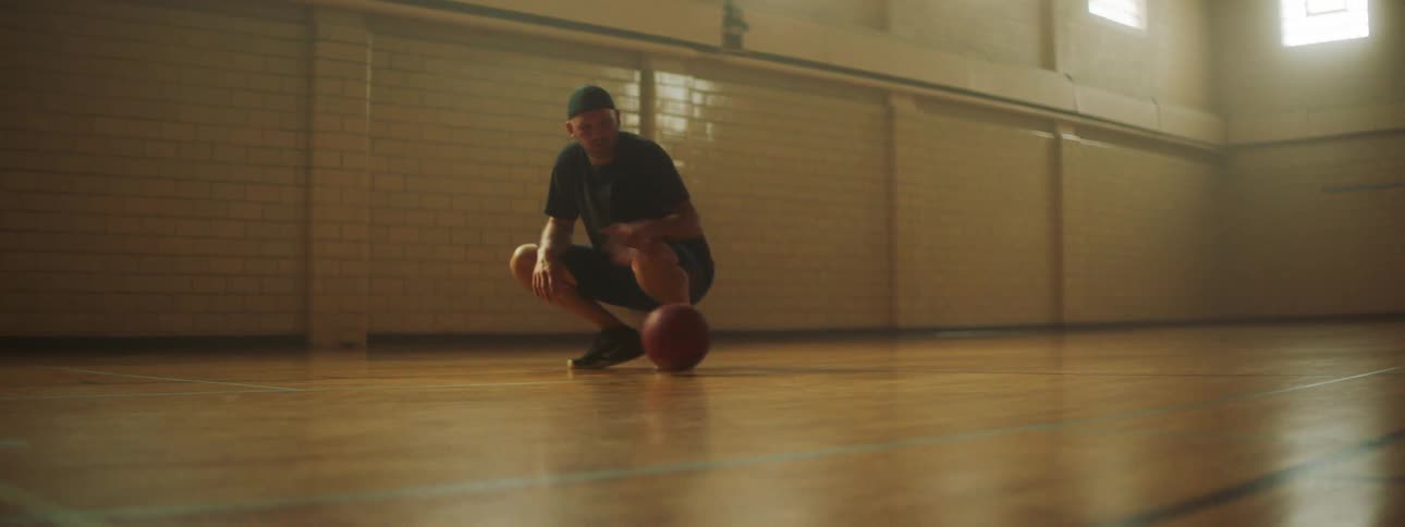 Man crouching on basketball court takes ball and smiles