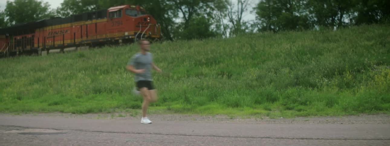 A jogger runs by as a train moves down an elevated track