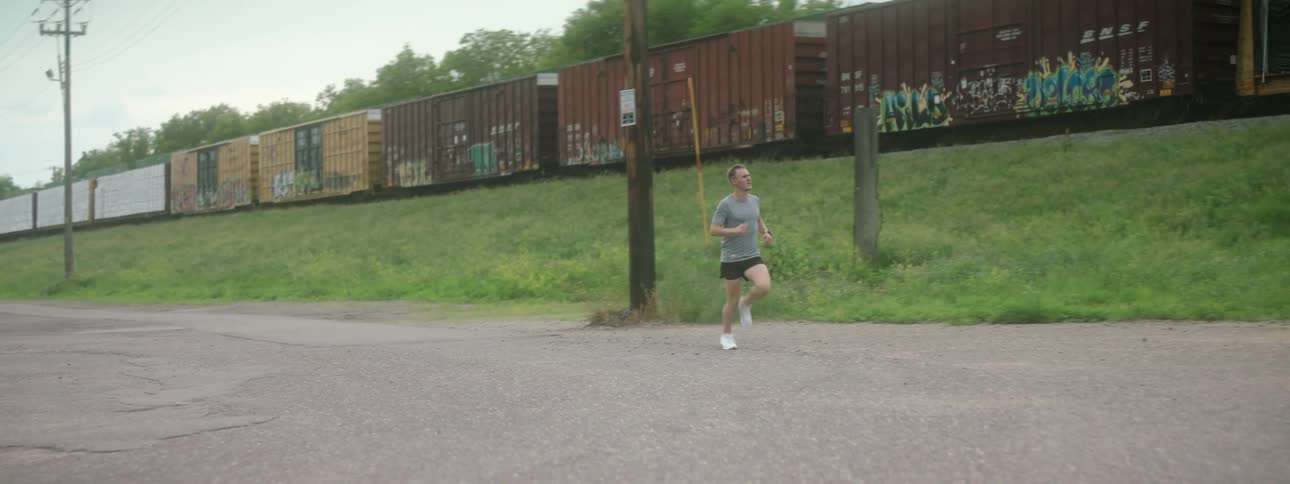 Man runs on alley alongside train tracks with freight train
