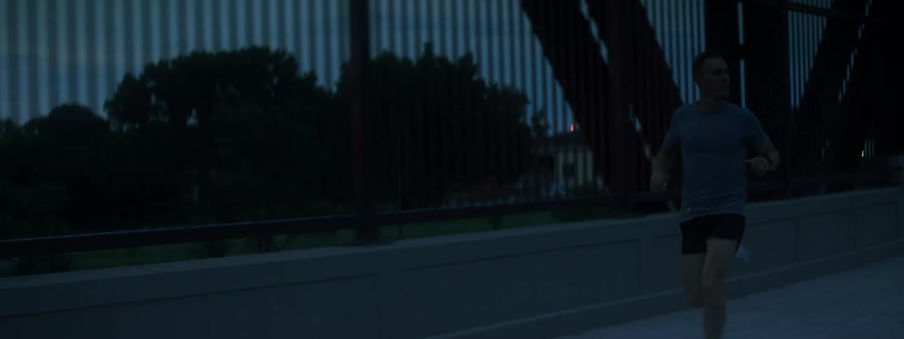 A male jogger running across a bridge just before sunrise