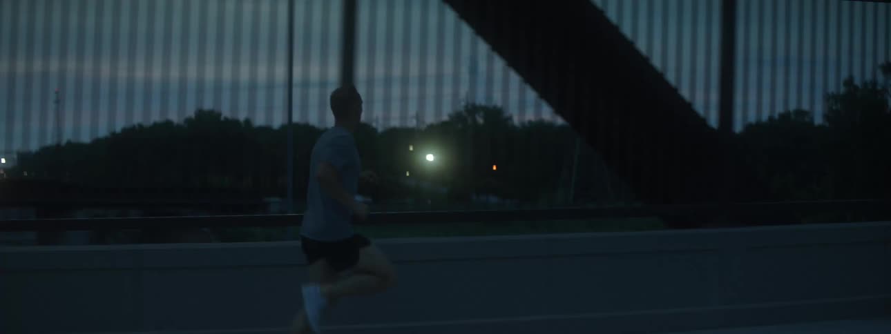 A man runs on the sidewalk of a bridge at night