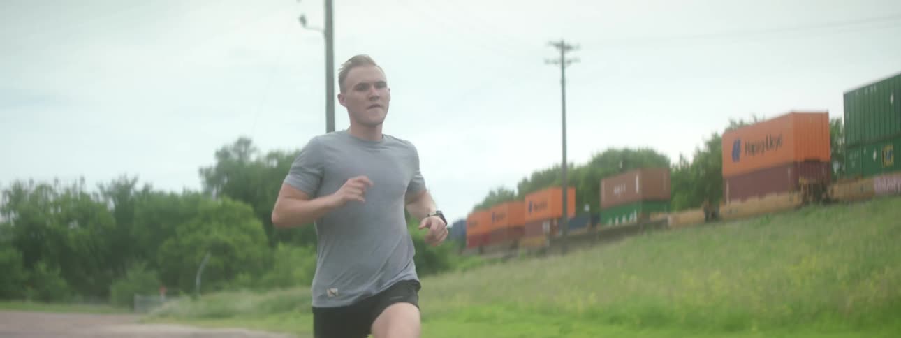 A man runs down a road as a train moves down the nearby tracks