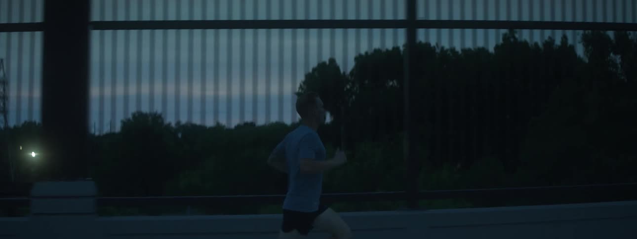 A man runs across a bridge with the city skyline behind him