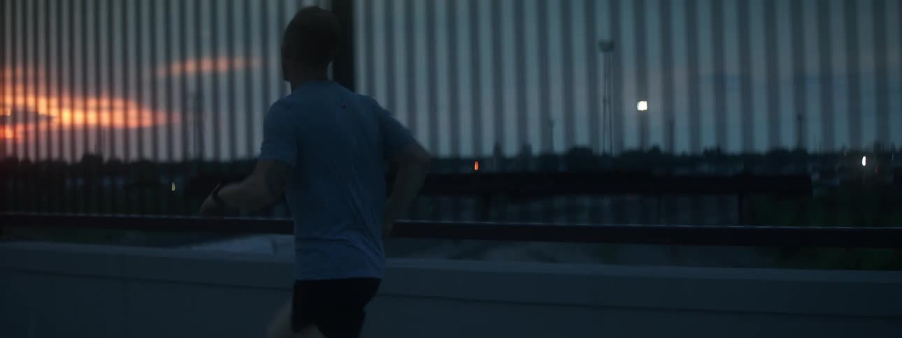 A jogger running across a bridge just before sunrise
